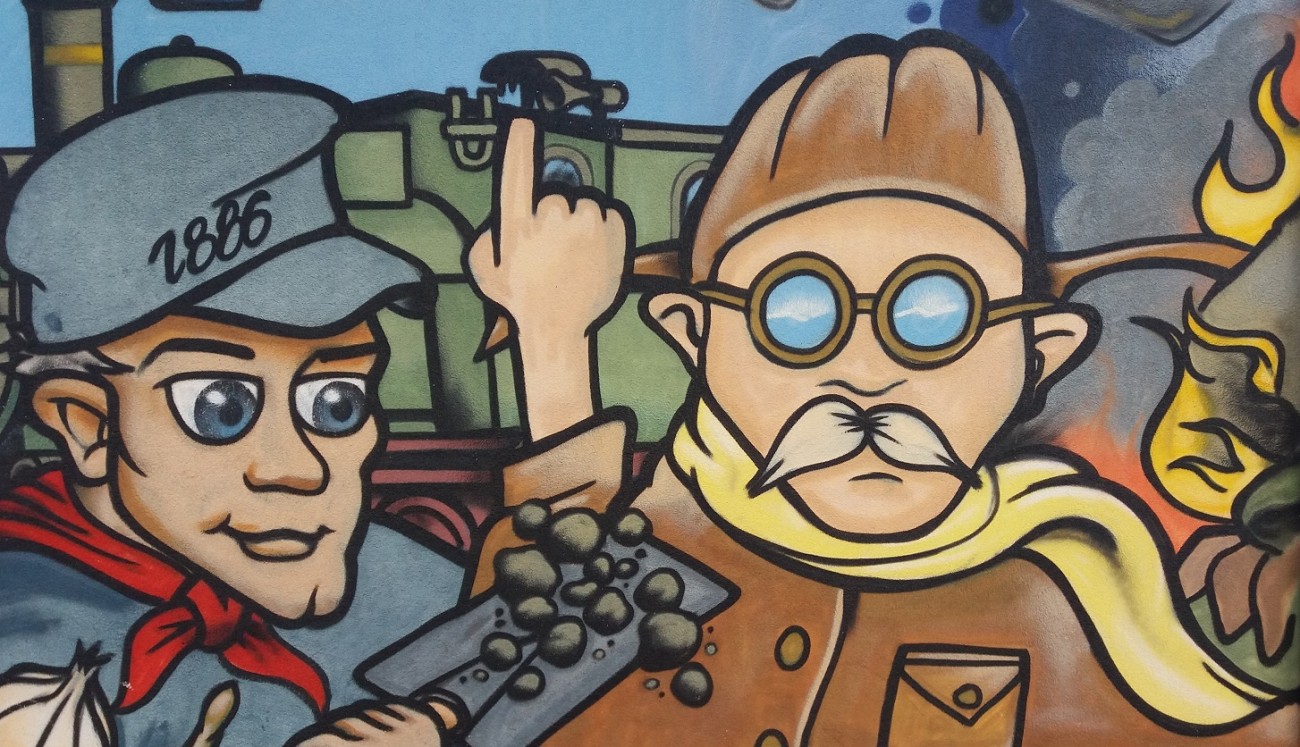 Graffito zur Ortsgeschichte, Griesheim, an der Wasserübergabestation Am Felsenkeller, gez. Kazu (S. Pieterse im Auftrag der Stadt Griesheim). Der Ausschnitt erinnert an den Bau der Dampfstraßenbahn zwischen Griesheim und Darmstadt 1886 und an den Flugpionier August Euler ("Flughafen" Griesheim 1908).